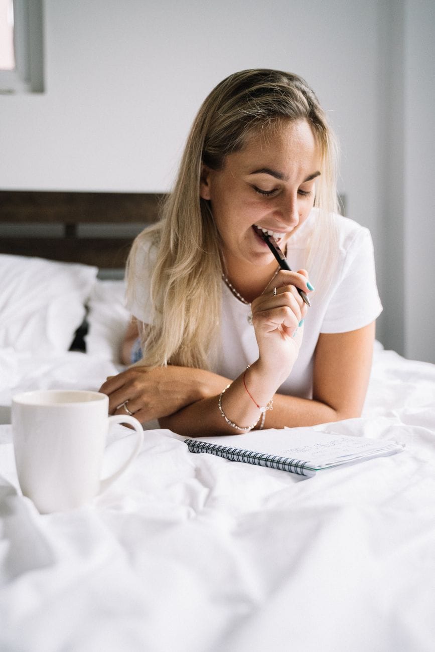 A woman writing in a notebook in bed with a morning coffee