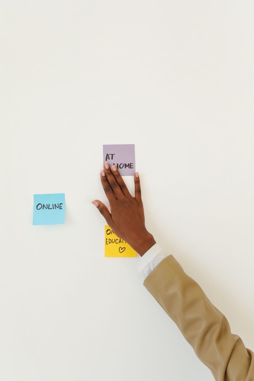 A hand arranging sticky notes reading 'online' and 'at home' on a wall