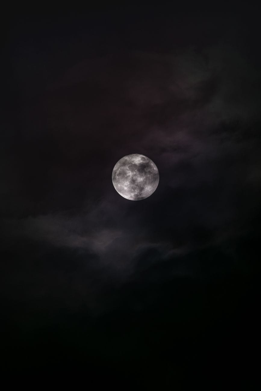 A full moon glowing through wisps of cloud in a dark sky