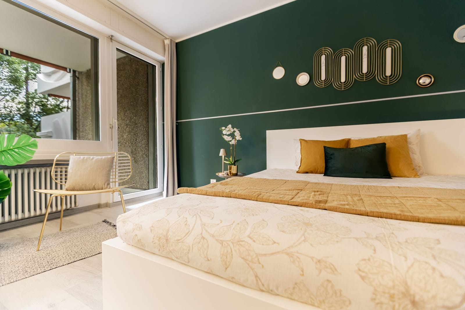 A bedroom with a deep emerald accent wall, gold art-deco decor, and warm ochre bedding