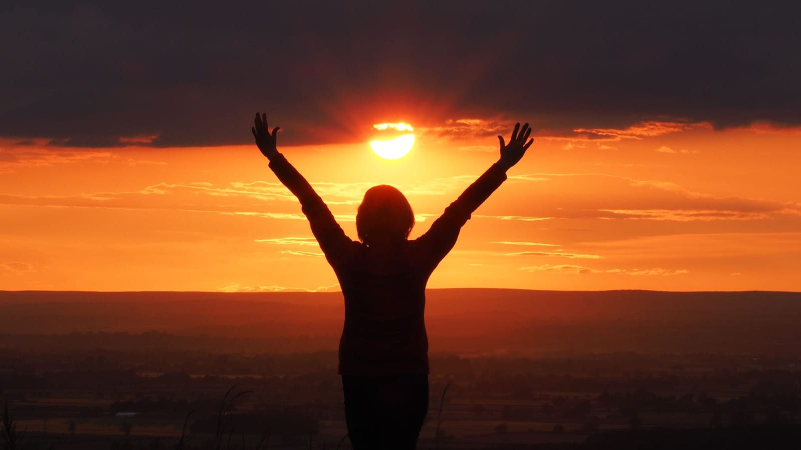 A woman raising her arms toward a sunset — the life a vision board helps you move toward